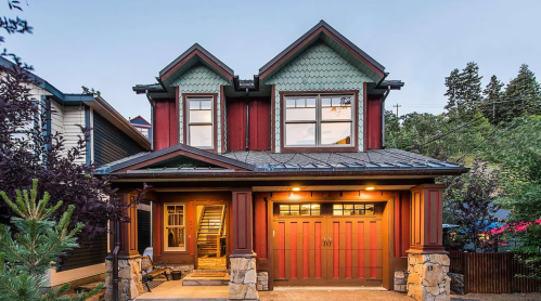 A charming two-story house with a red and green exterior, featuring large windows and a stone-accented entrance.